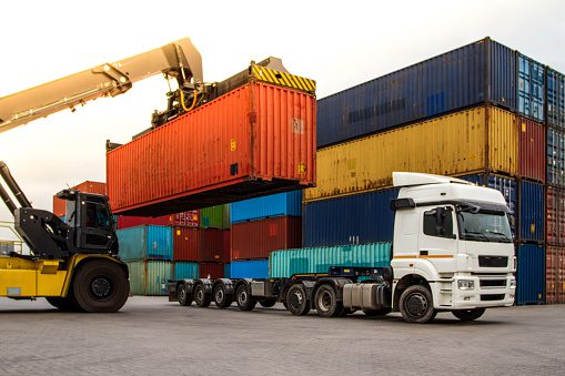 Truck while loading in logistic shipping yard with cargo container. Forklift truck handling truck. Logistic import export concept. Loading and unloading of containers in the port.